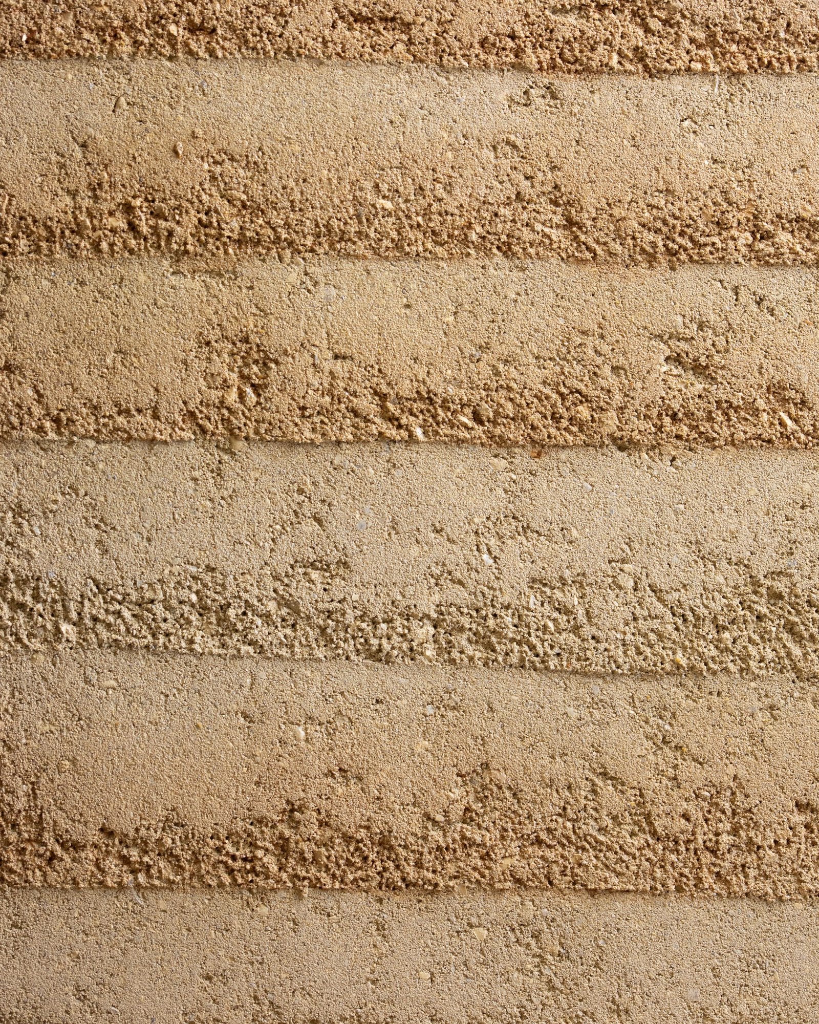 Rammed earth finish showing horizontal strata banding in warm earth tones.