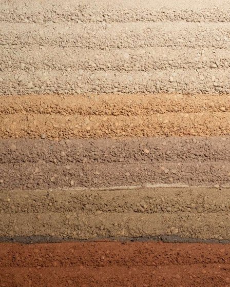 Rammed earth showing full strata banding from cream through ochre to terracotta.