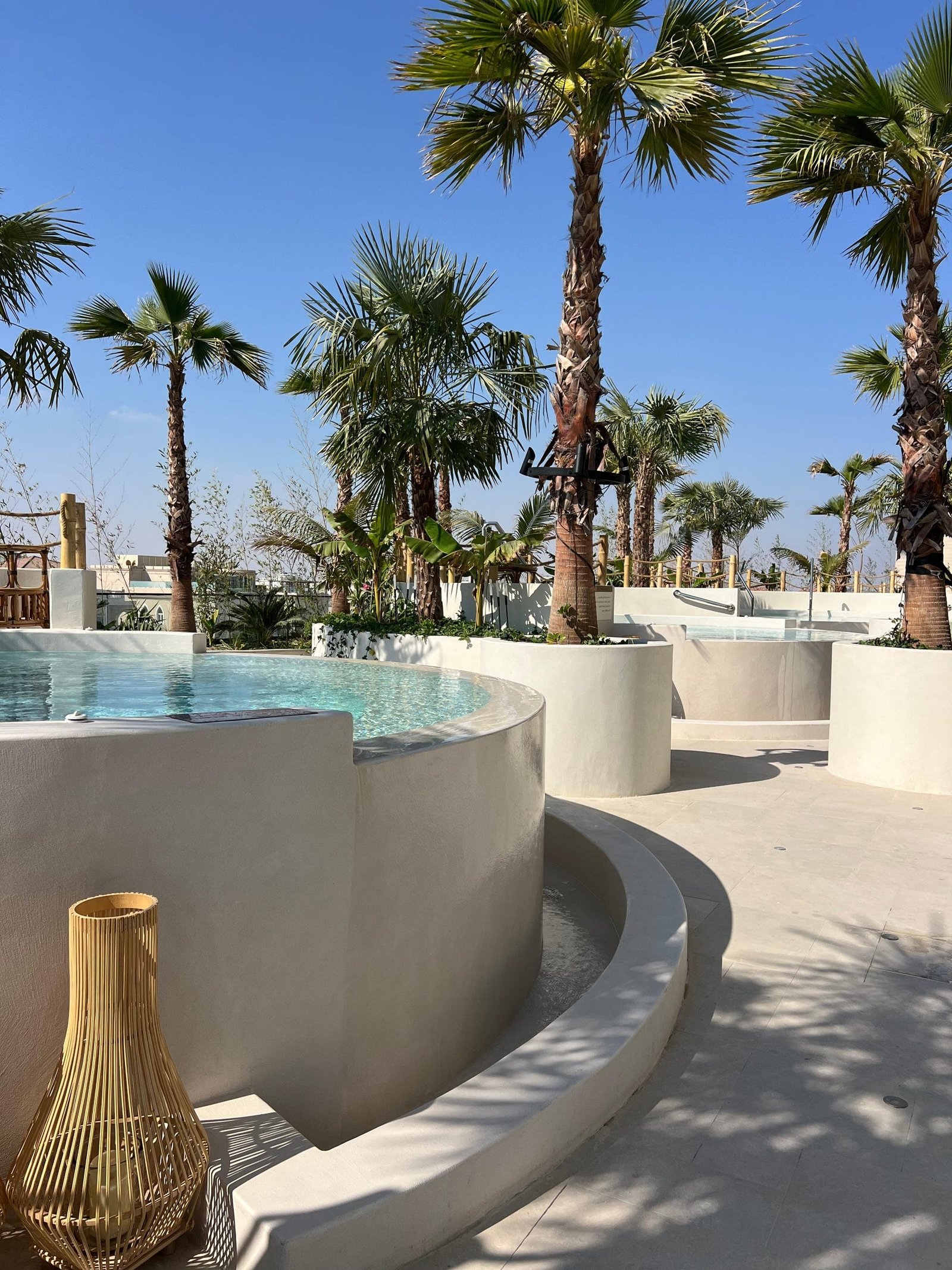 Curved microcement pool surround and planters at The OQ Hotel, Doha, meeting turquoise water under palms