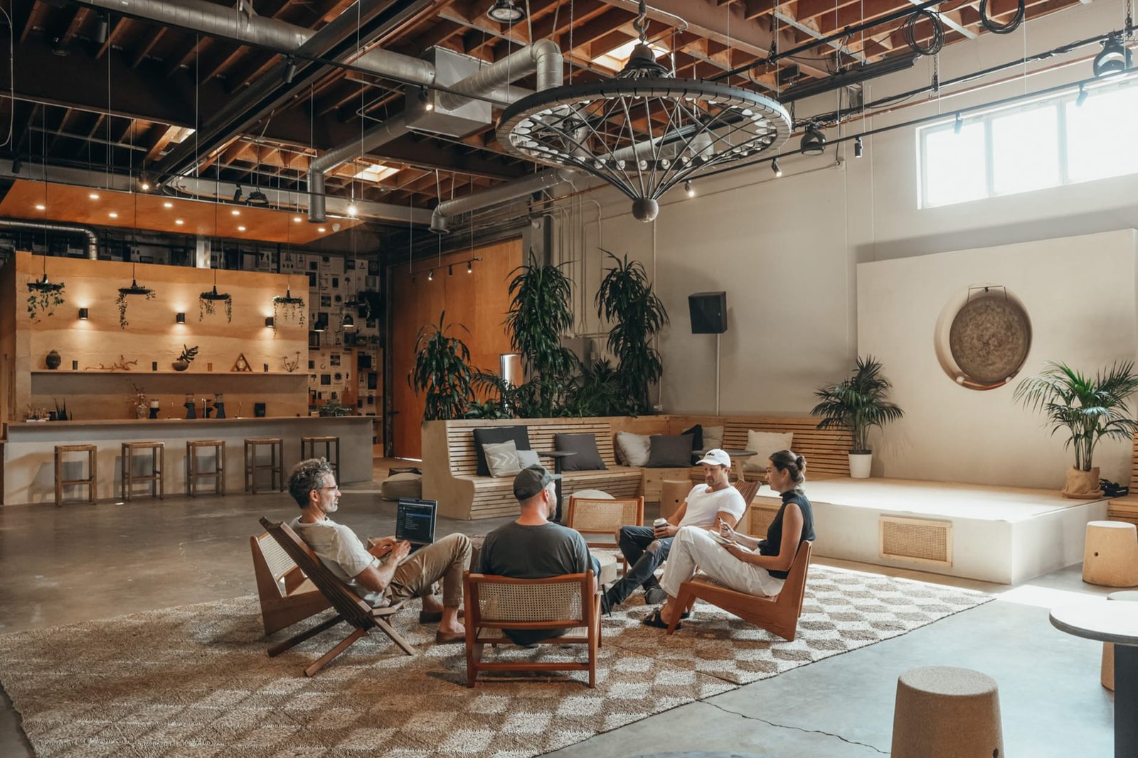 Wide view of MUD\WTR Gather: the Rammed Earth bar at left, a wheel chandelier and a circle of cane chairs.