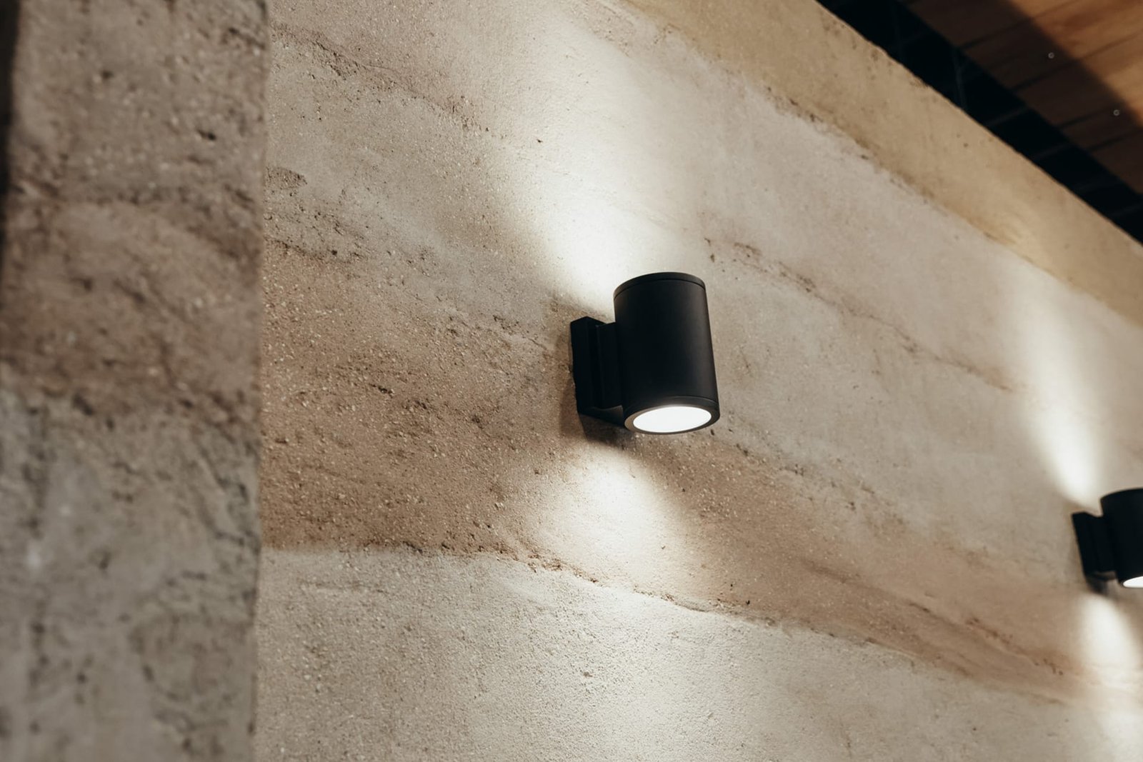 Detail of the Rammed Earth finish at MUD\WTR Gather, strata bands raking under a black wall light.