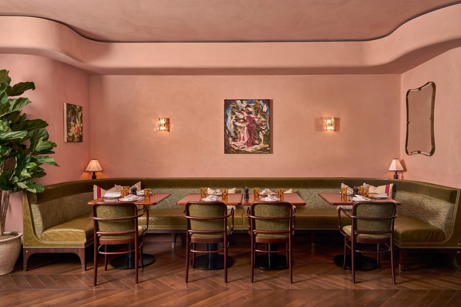 Curved banquette at Nipotina against smooth nude clay plaster hung with art, flanked by glass sconces.