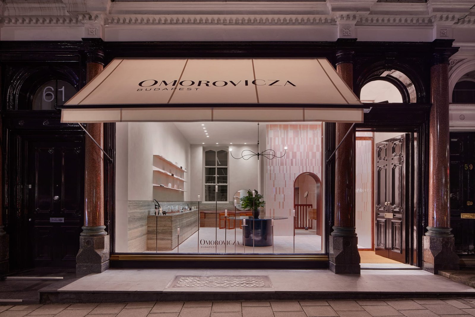 Omorovicza Mayfair shopfront at night, awning above the glazed frontage with the clay-plastered interior lit within.