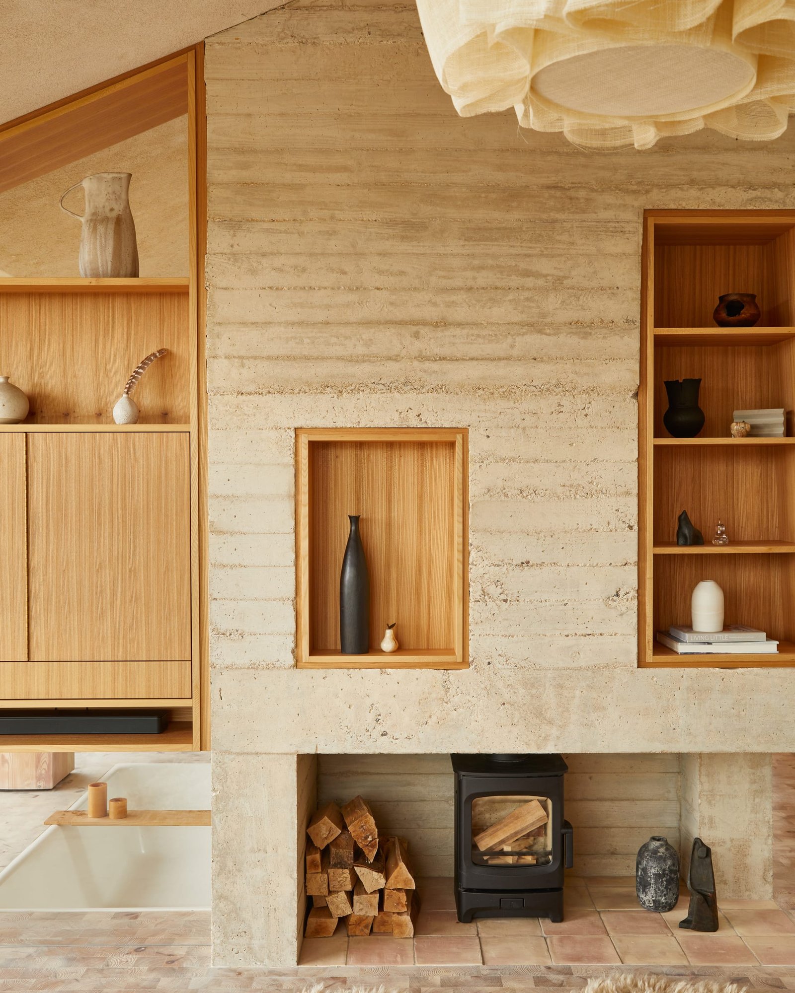 Central concrete fireplace and chimney at The Makers Barn with elm shelving niches and a wood-burning stove.