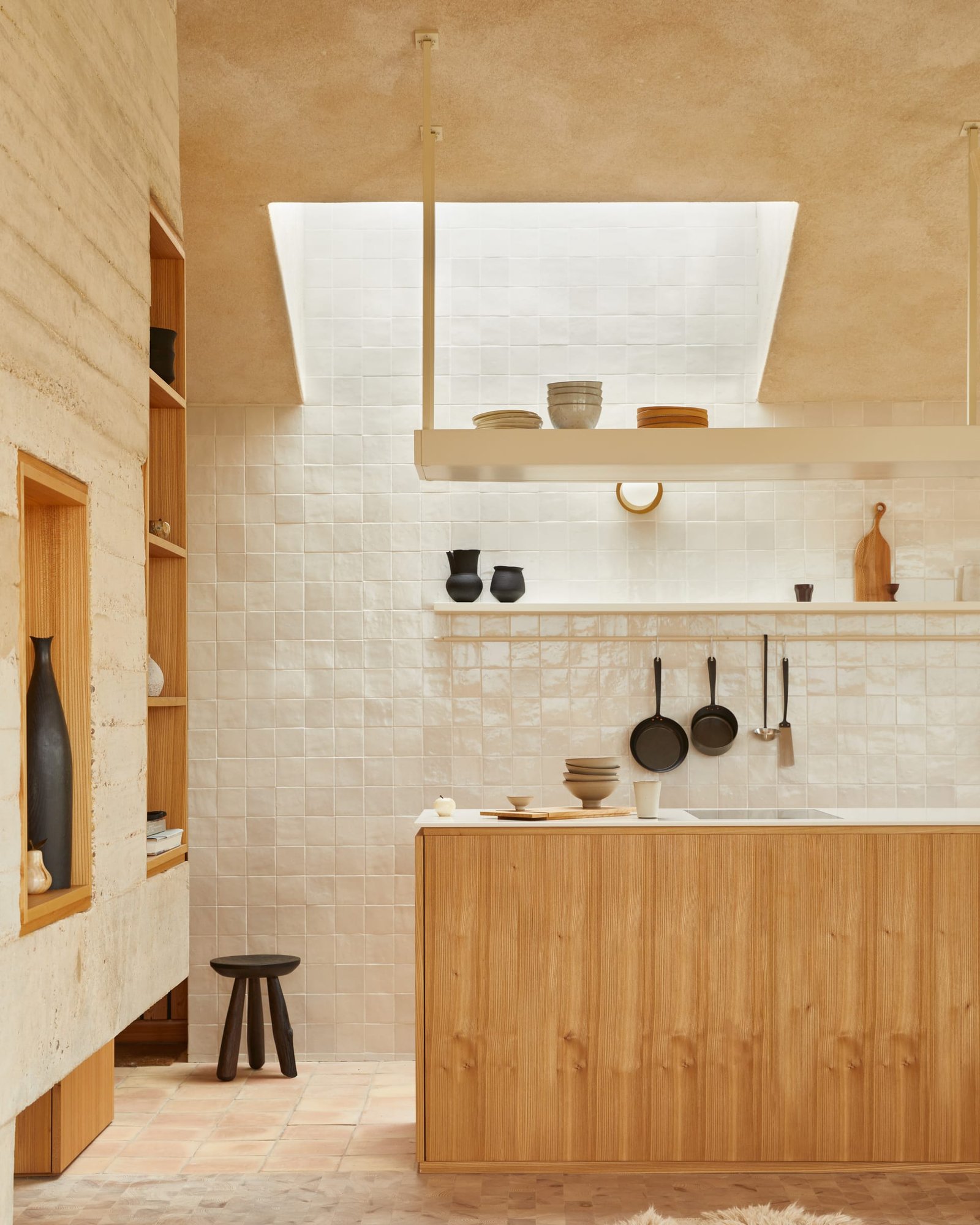 Kitchen at The Makers Barn: clay-plastered ceiling and shuttered concrete wall beside a fluted timber island and zellige tiling.