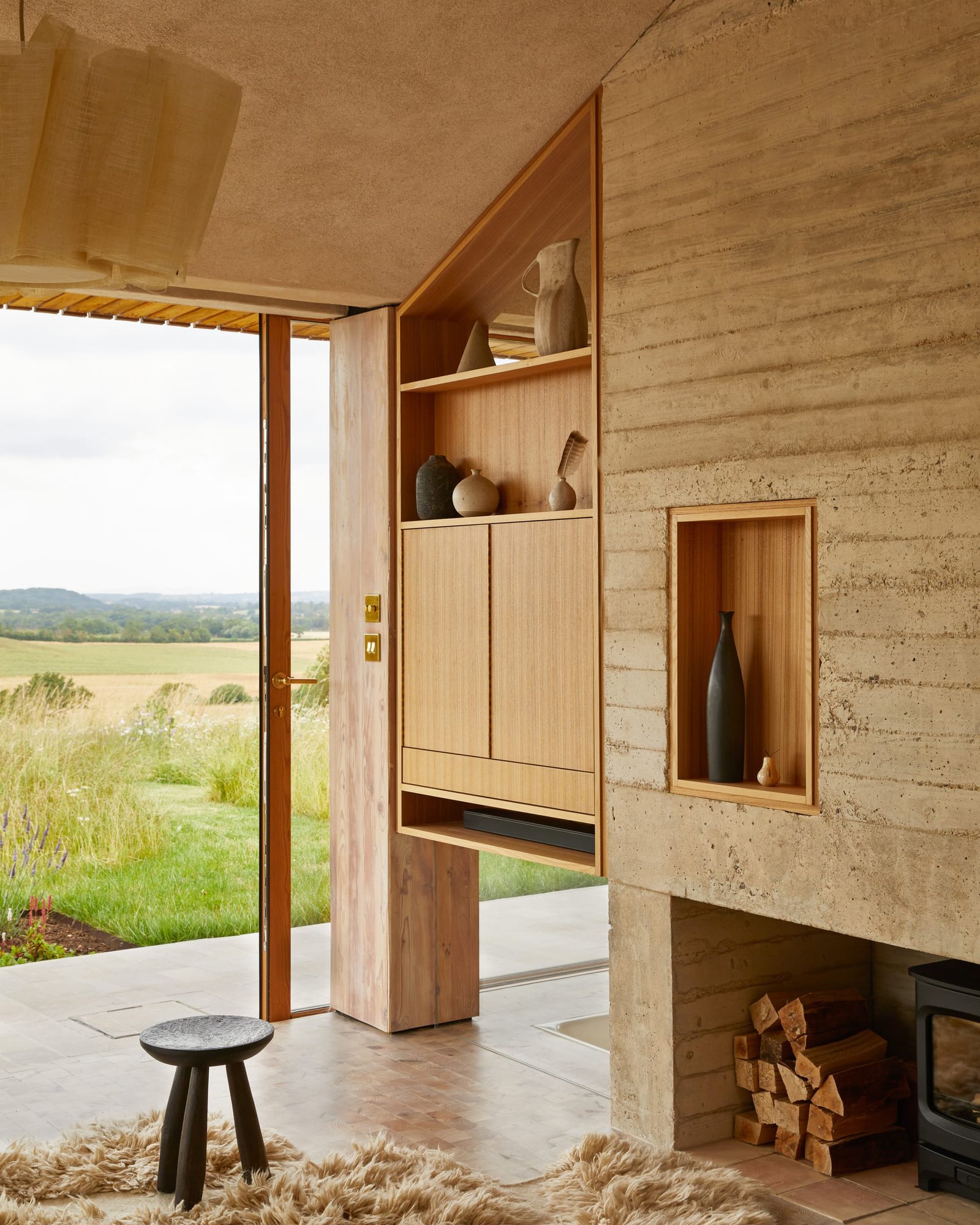 Doorway at The Makers Barn opening onto the meadow, clay-plastered ceiling and shuttered concrete beside elm joinery.