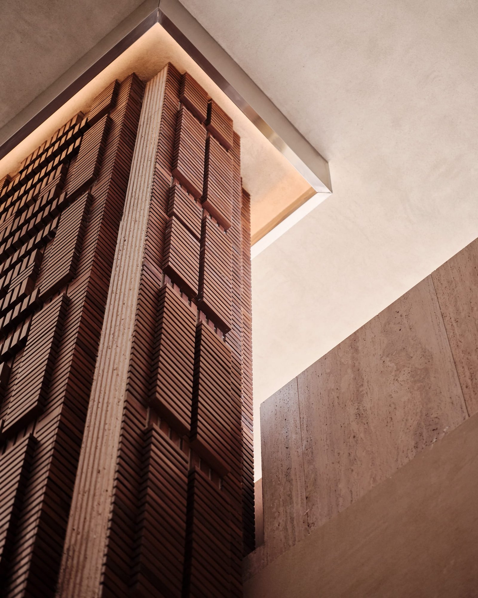 Looking up at the twelve-metre timber structure at Toplum against clay-plastered and travertine surfaces.