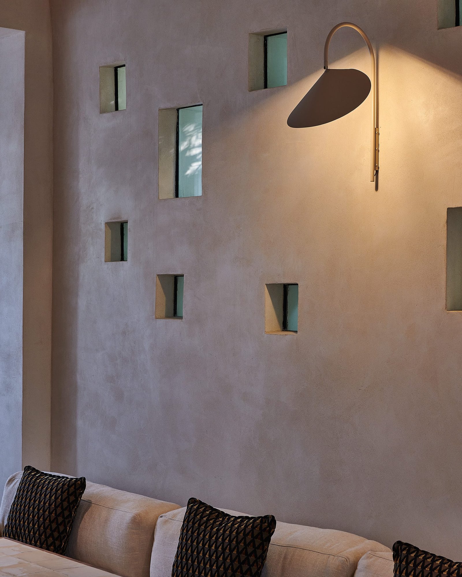 Smooth white clay plaster wall at Villa 515 with punched openings and a wall light casting a soft pool of light.