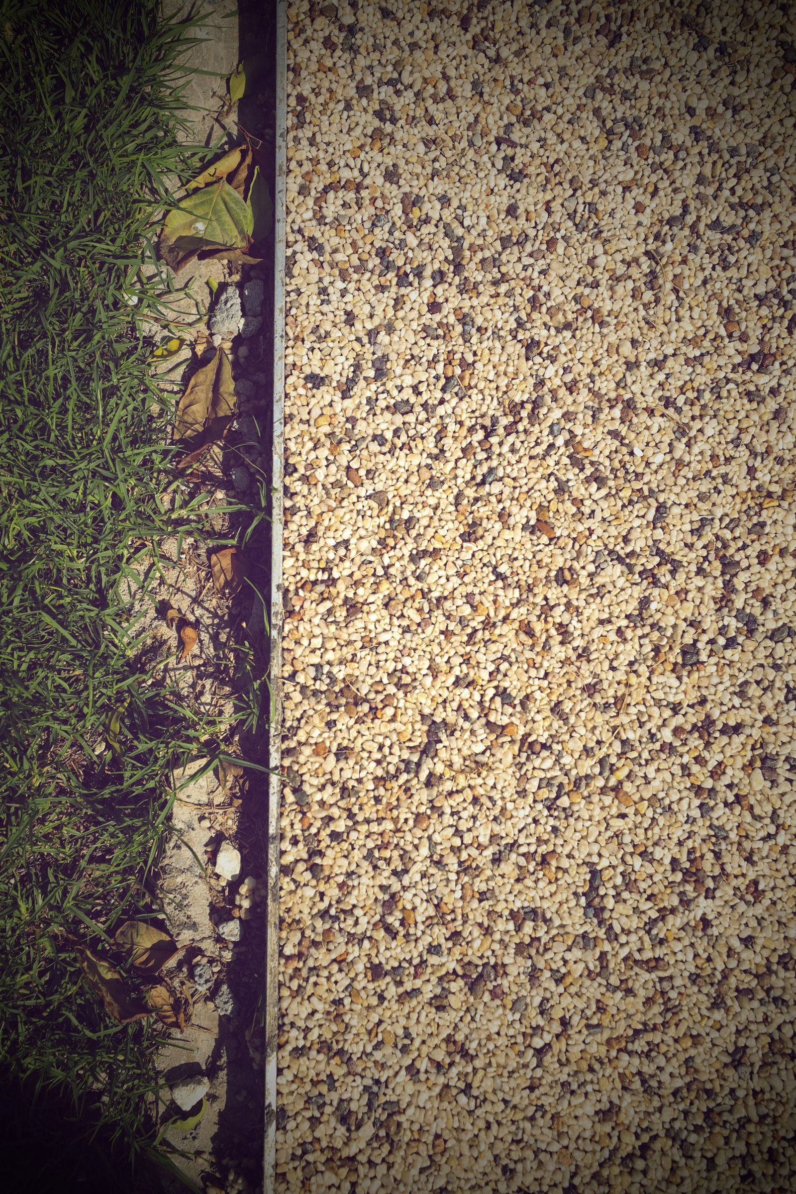Top-down detail of cream and grey resin-bound aggregate walkway meeting a metal edging strip and grass planting strip.