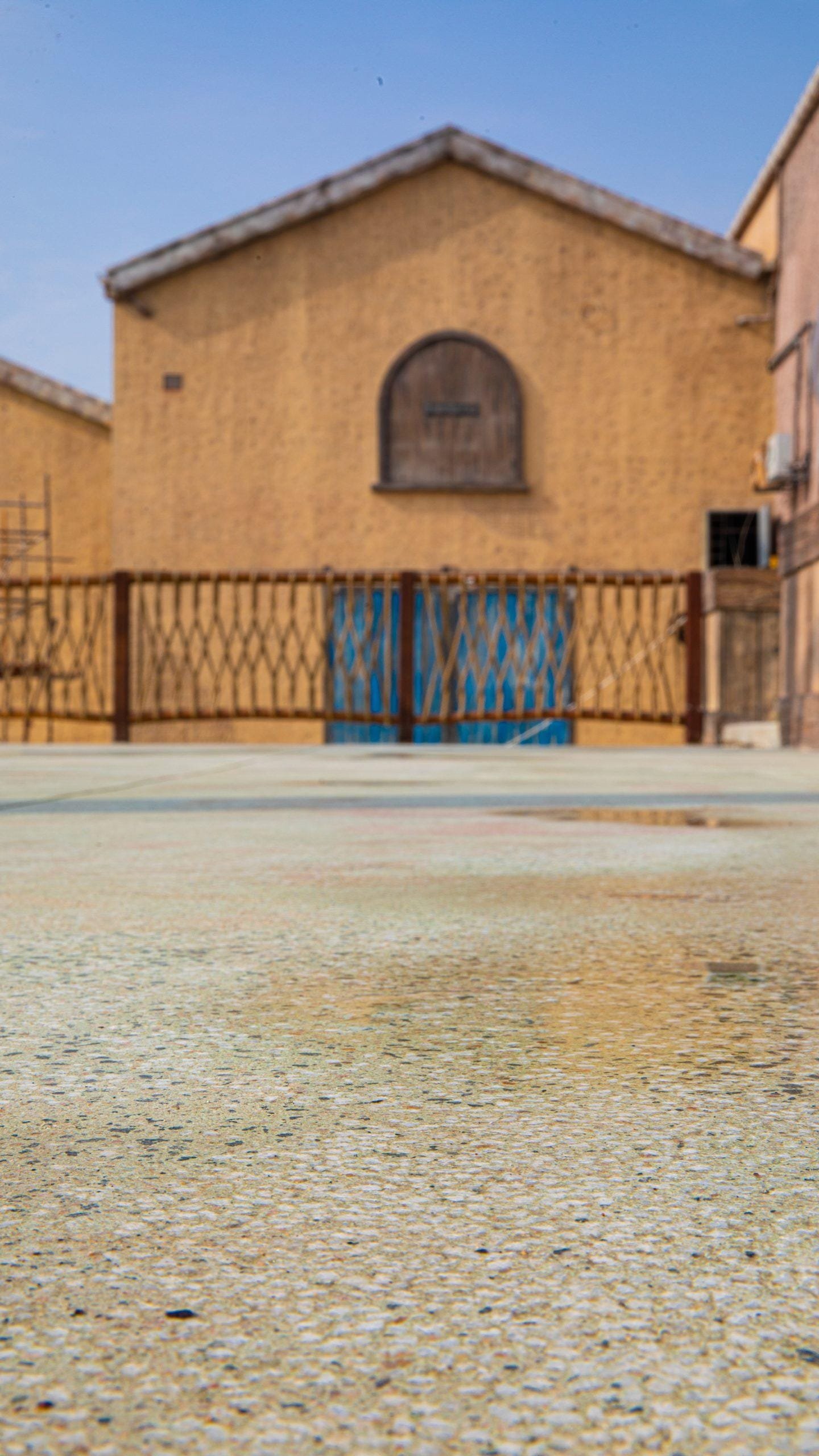 Pale sage-green exposed aggregate plaza deck in front of an ochre barn-style building at Meryal Waterpark
