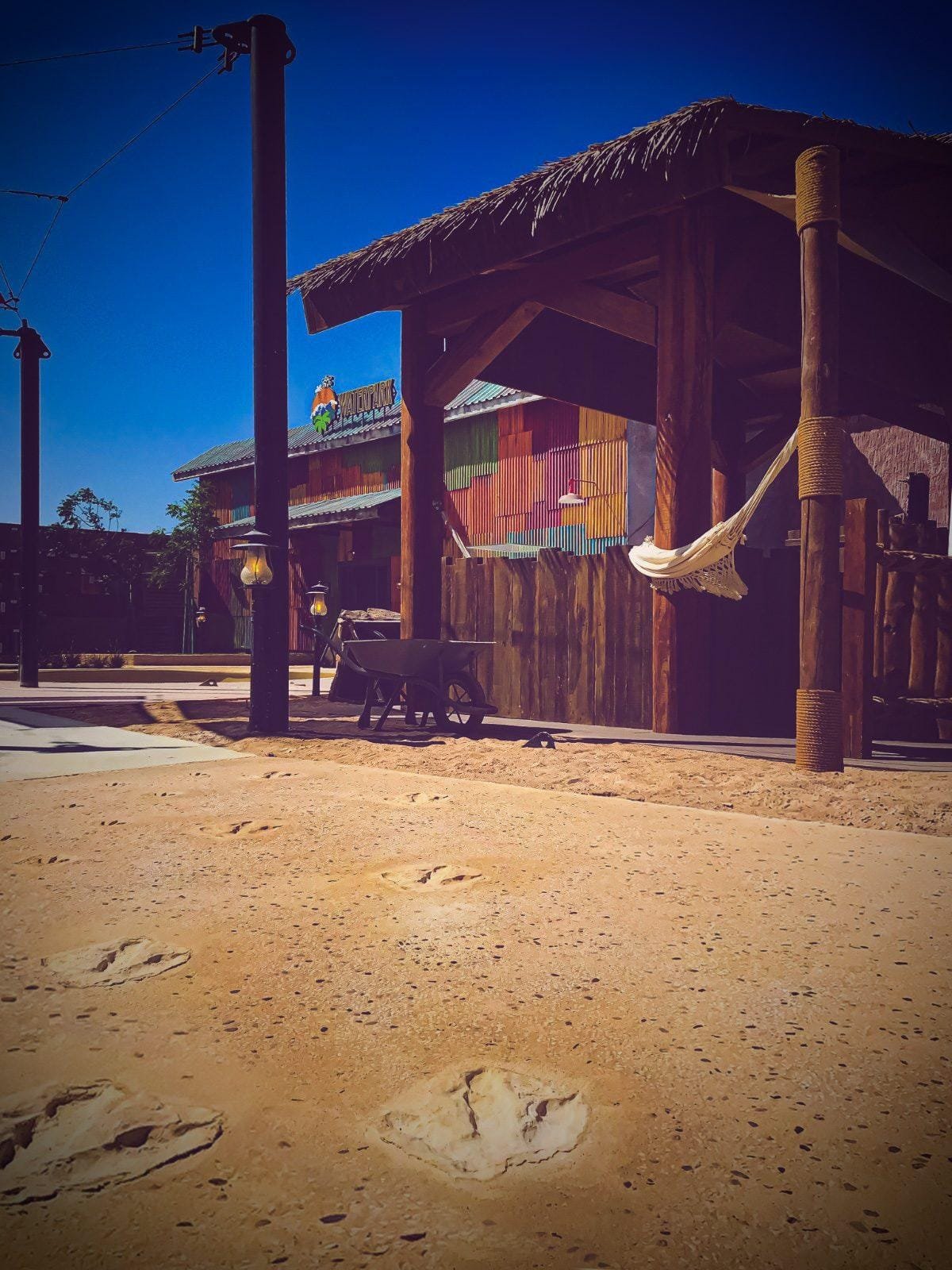 Dinosaur footprints imprinted in ochre exposed aggregate concrete leading past a thatched timber pavilion at Meryal Waterpark