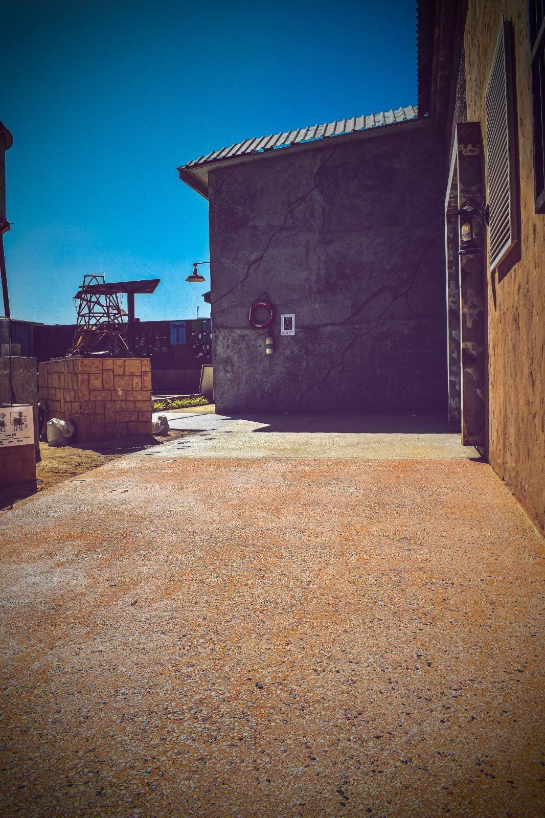 Rust-red speckled exposed aggregate walkway between an ochre building and a dark rendered wall at Meryal Waterpark