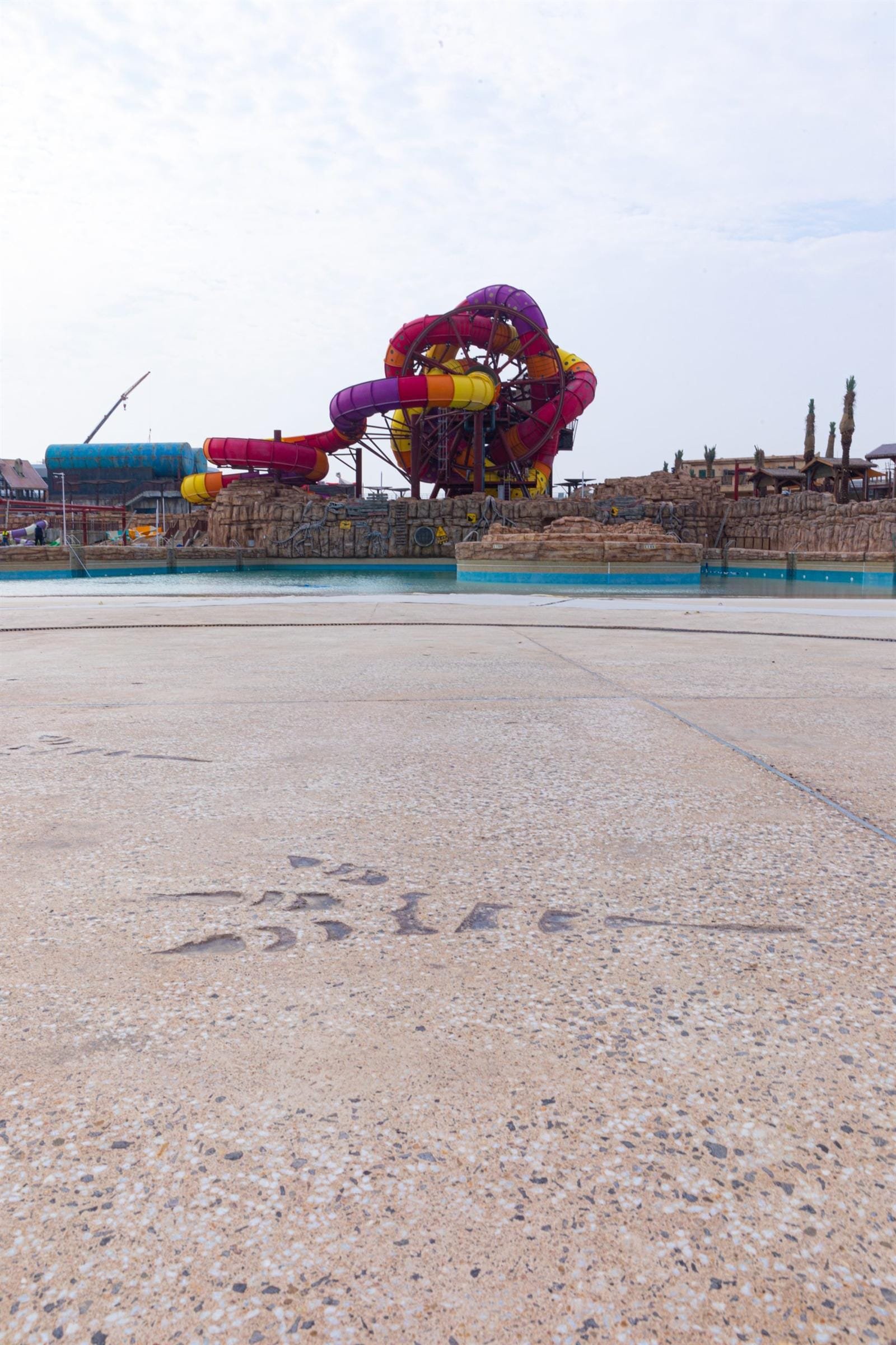 Wave pool deck in pale sand Exposed Plus exposed aggregate concrete with imprinted dinosaur footprint trails at Meryal Waterpark, Qetaifan Island