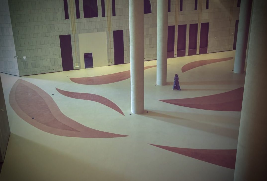 Monumental hall at King Fahad Cultural Centre, Riyadh, with dusty-rose leaf inlays sweeping across cream Microdur Plus microcement flooring around massive columns.