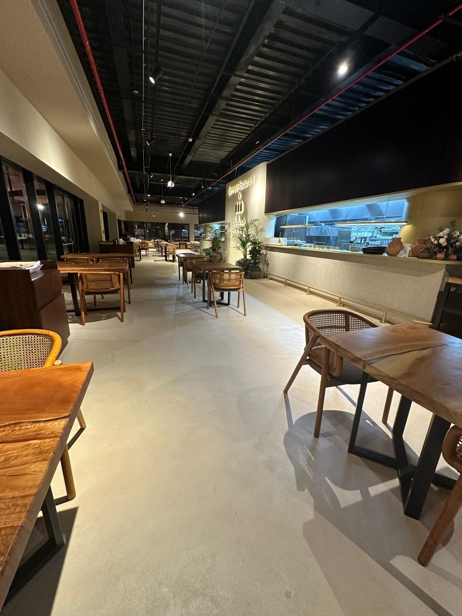 Biennale Restaurant dining hall in Jeddah at night, a pale seamless Microdur Plus microcement floor with timber tables