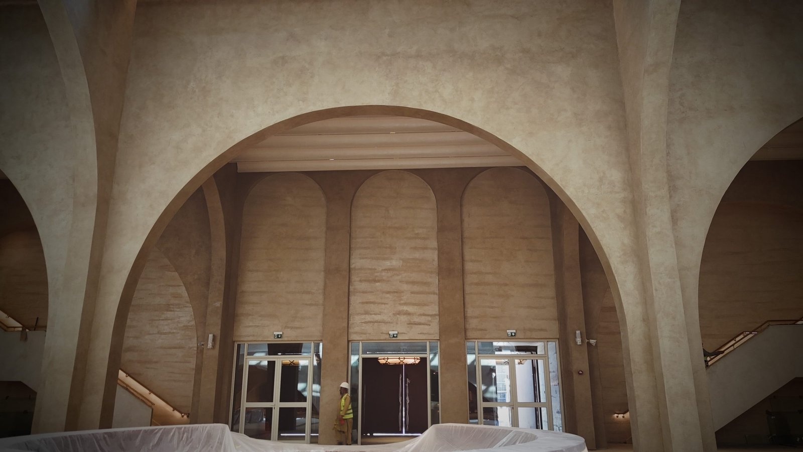 Broad plaster arch framing three arched bays above glazed entrance doors, sand-beige tadelakt throughout, sheeted counters