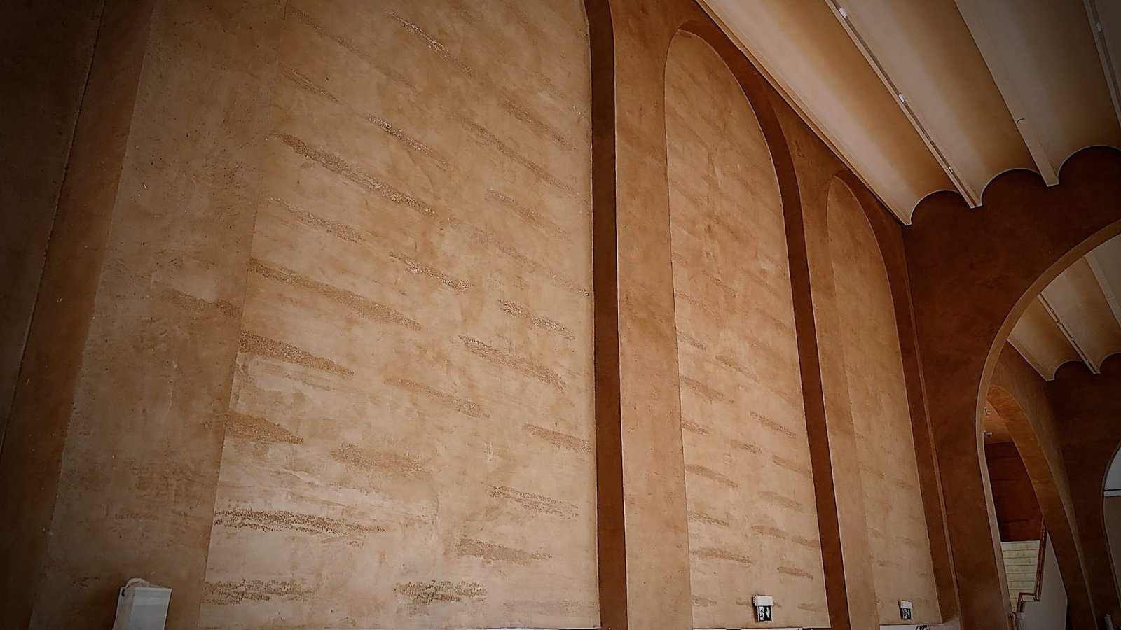 Tall wall of arched-top recessed panels between pilaster bands in terracotta striated plaster, scalloped white ceiling edge