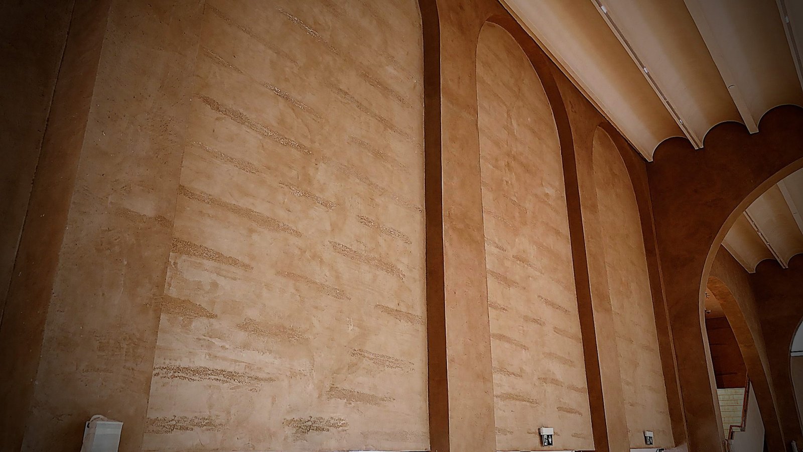 Tall wall of arched-top recessed panels between pilaster bands in terracotta striated plaster, scalloped white ceiling edge