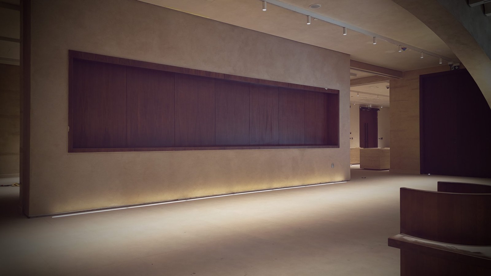 Gallery with a long recessed dark-timber display niche set in a sand plaster wall, LED underglow at the base, track lighting