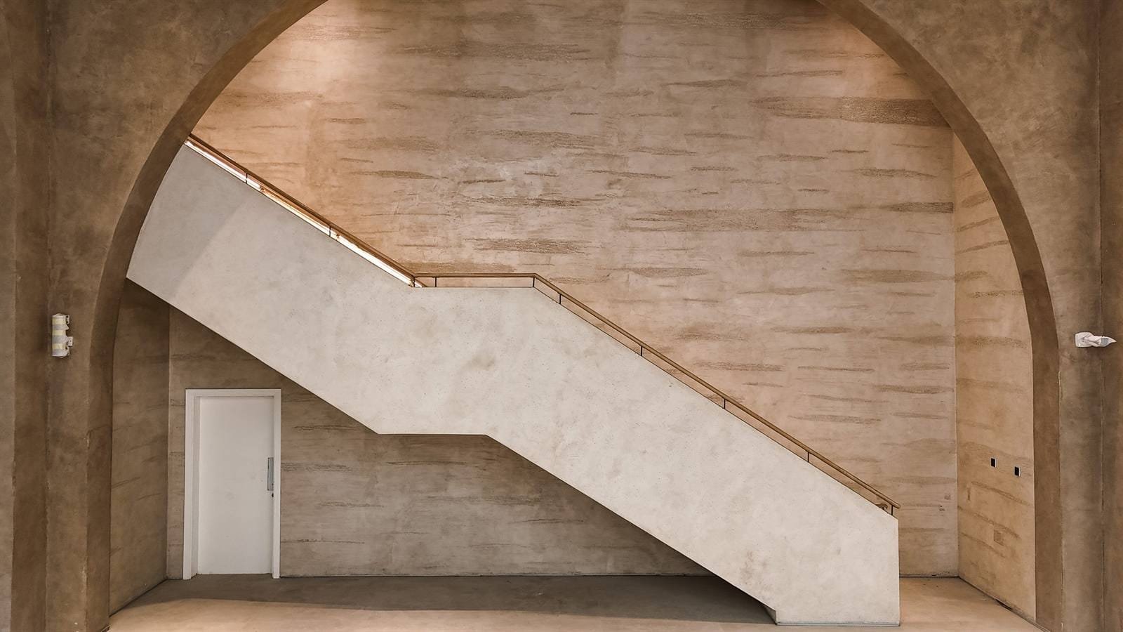 Symmetric view through an arch of a straight stair with pale plaster balustrade and timber rail against a striated