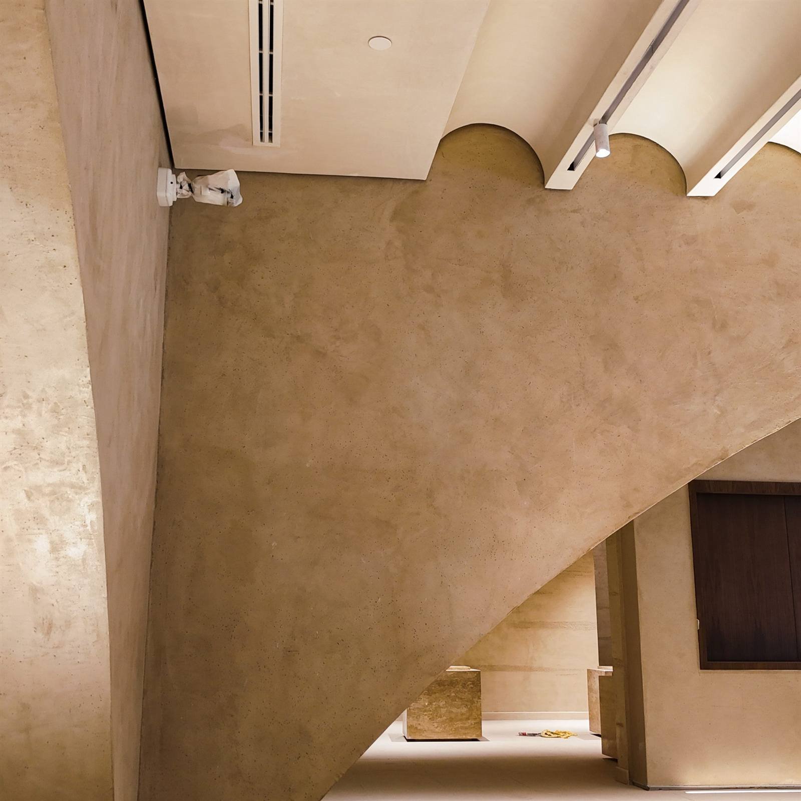 Sweeping curved stair soffit in sand Microtadelakt meeting scalloped arch heads and a white ceiling band with linear