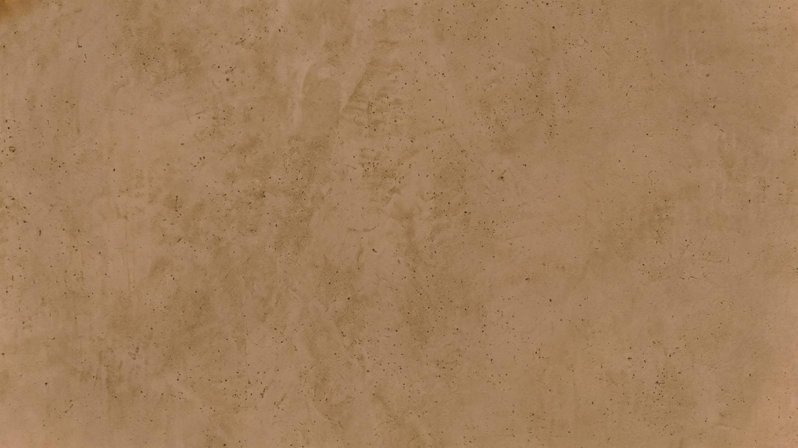 Full-frame close-up of the same speckled sand plaster surface in a warmer caramel grade, pinhole pores and trowel clouding