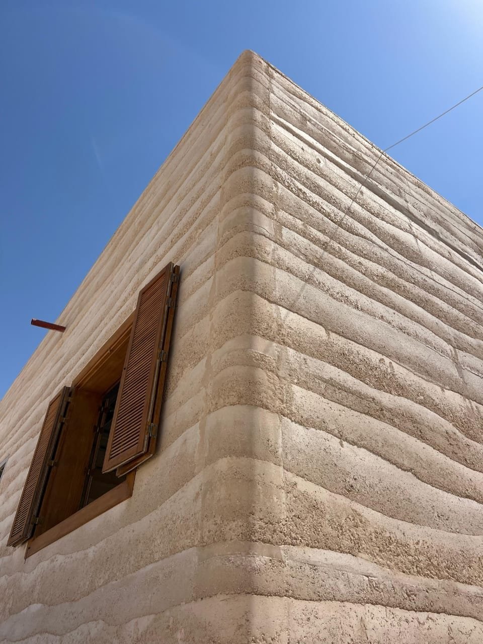 Close corner detail of an in-situ rammed earth wall at Al Kaaban Resort, Qatar, showing tamped lifts against a blue sky