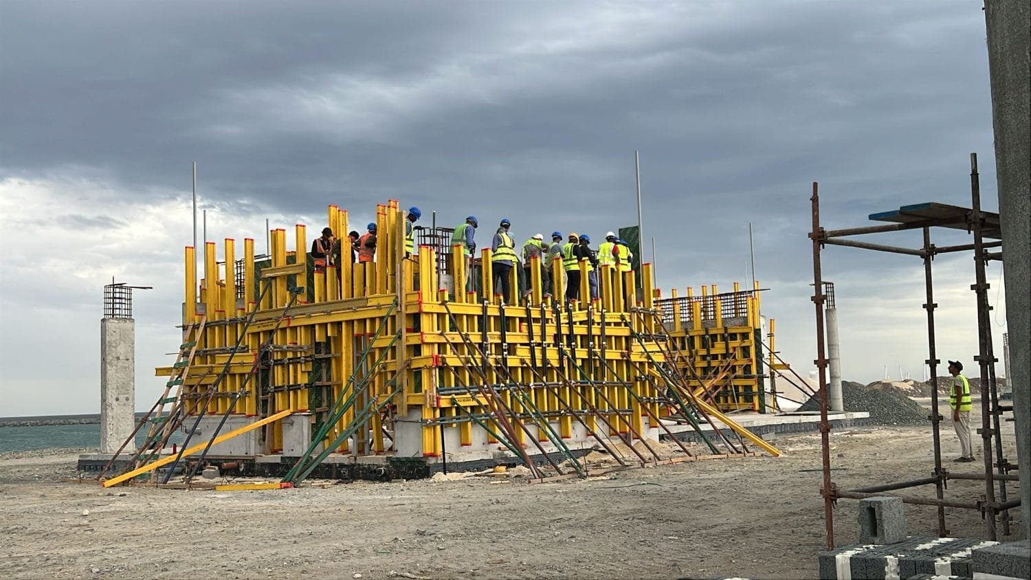 Long run of yellow H20 formwork with raking props at Kalba Beach, crews working along the top of the wall