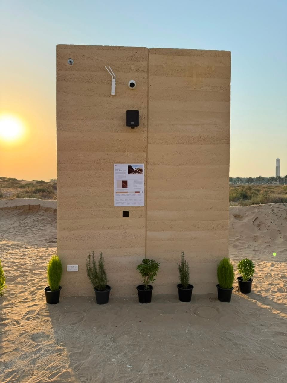 Rammed earth site mock-up wall at Kalba Beach, Sharjah, at sunset with the specification board fixed to it