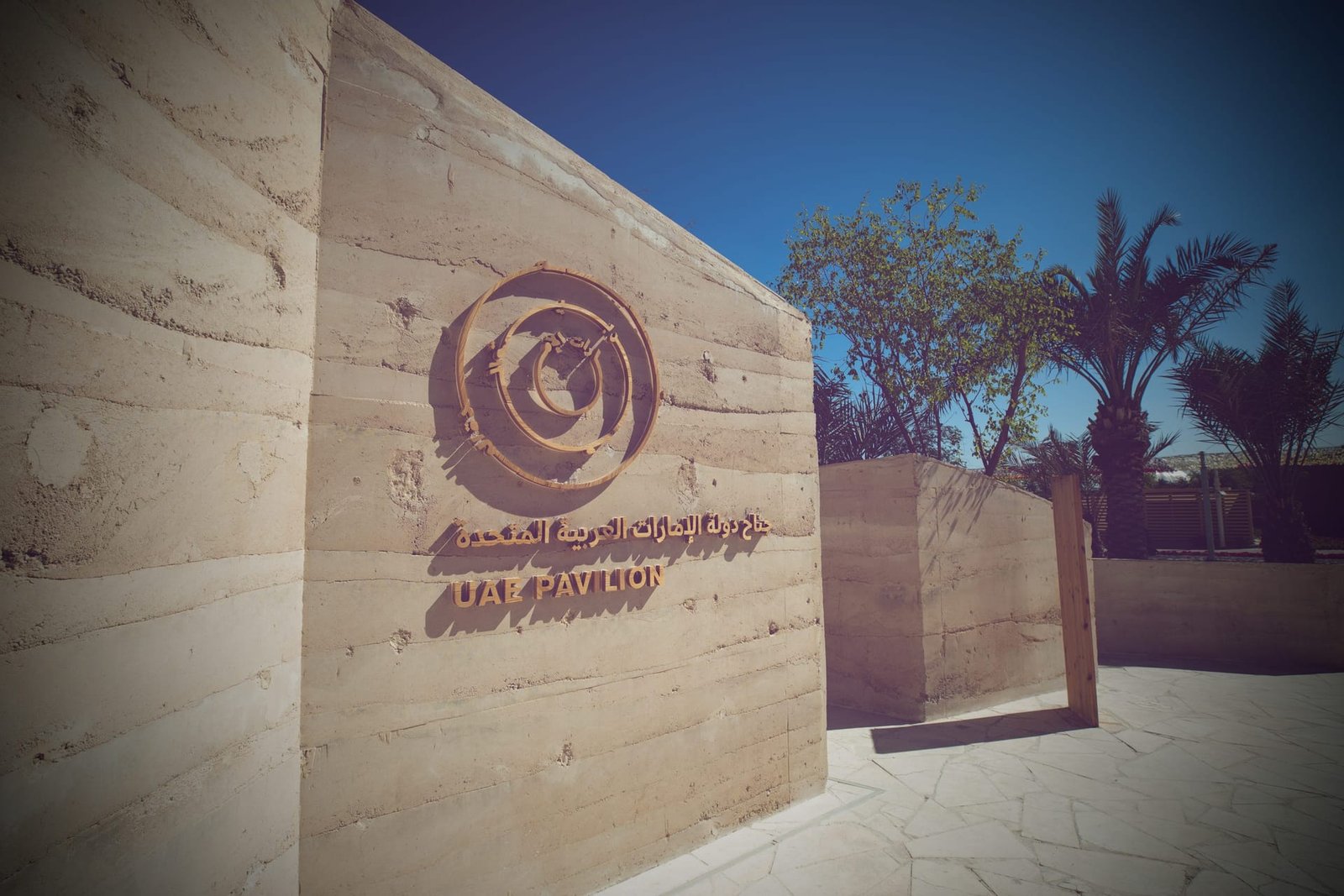 Rammed earth entrance wall of the UAE Pavilion carrying its carved timber emblem and lettering
