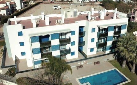 Aerial view of a white apartment block with projected cork roof terraces and a pool below