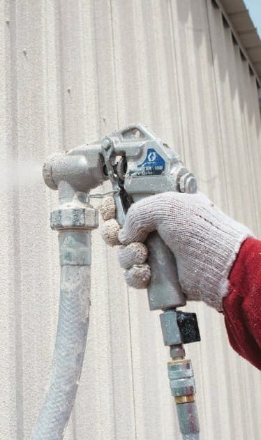 Gloved hand holding the spray gun used to apply projected cork to a wall