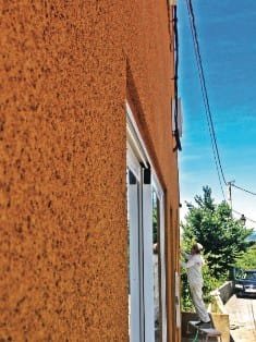 Applicator spraying ochre projected cork onto a house facade beside a window