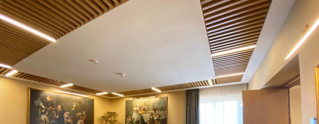 Seamless acoustic plaster ceiling panel framed by timber slats in a meeting room at Banca d’Italia, Rome