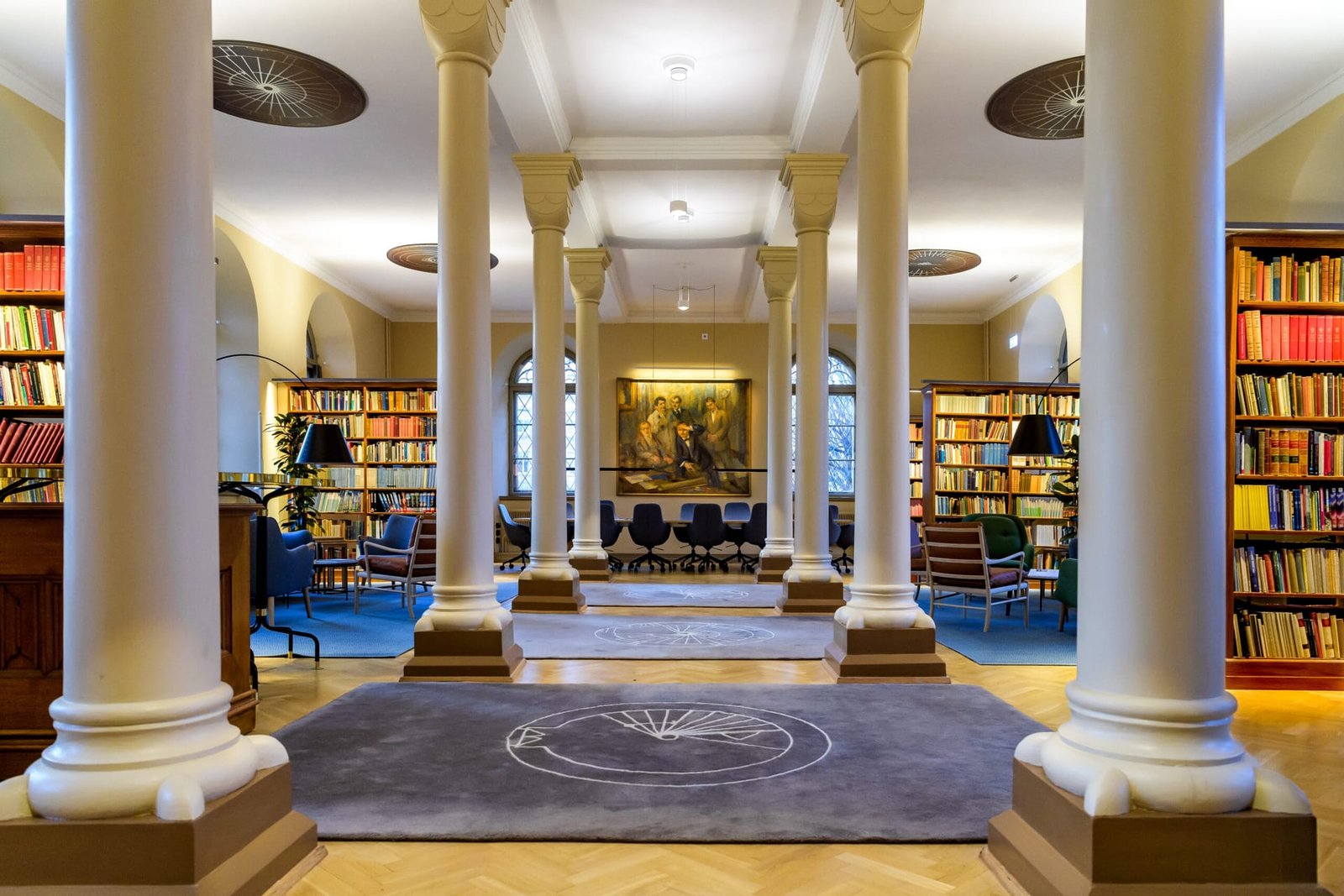 Historic reading room with white columns, full-height bookcases and dark circular acoustic medallions set into the ceiling