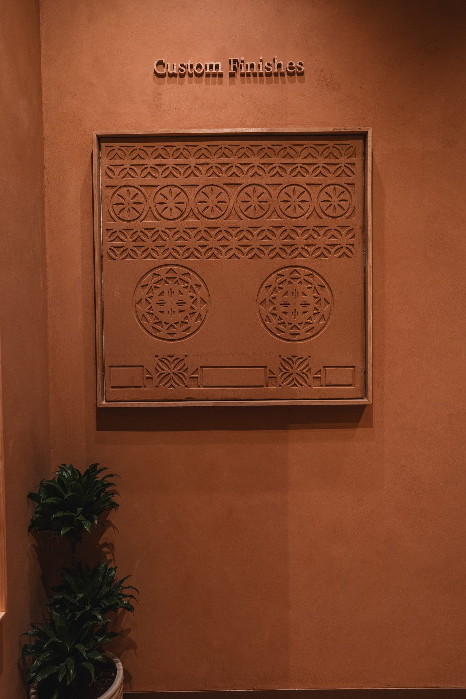 Custom Finishes panel at the Conmarble showroom: a framed terracotta clay plaster relief carved with Najdi geometric bands and rosettes.