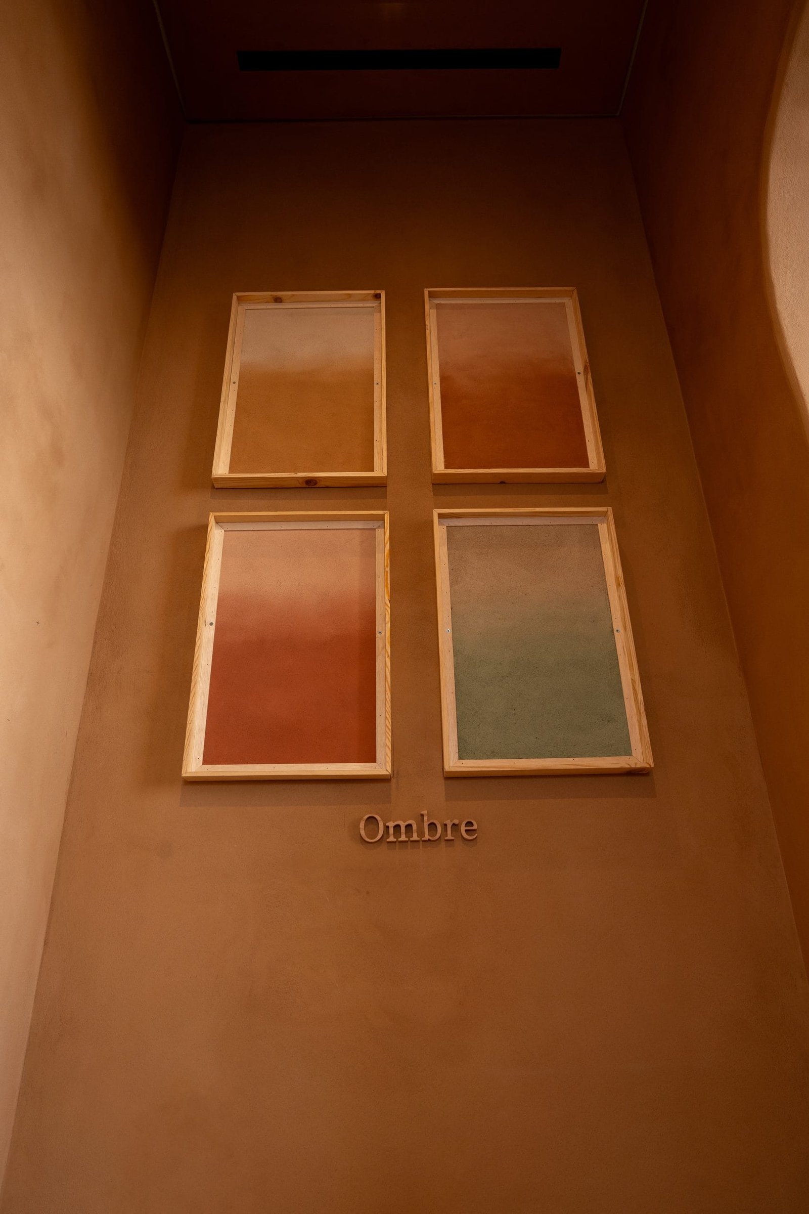 Ombre sample wall at the Conmarble showroom: four framed clay plaster panels graded from ochre and terracotta to sage green.