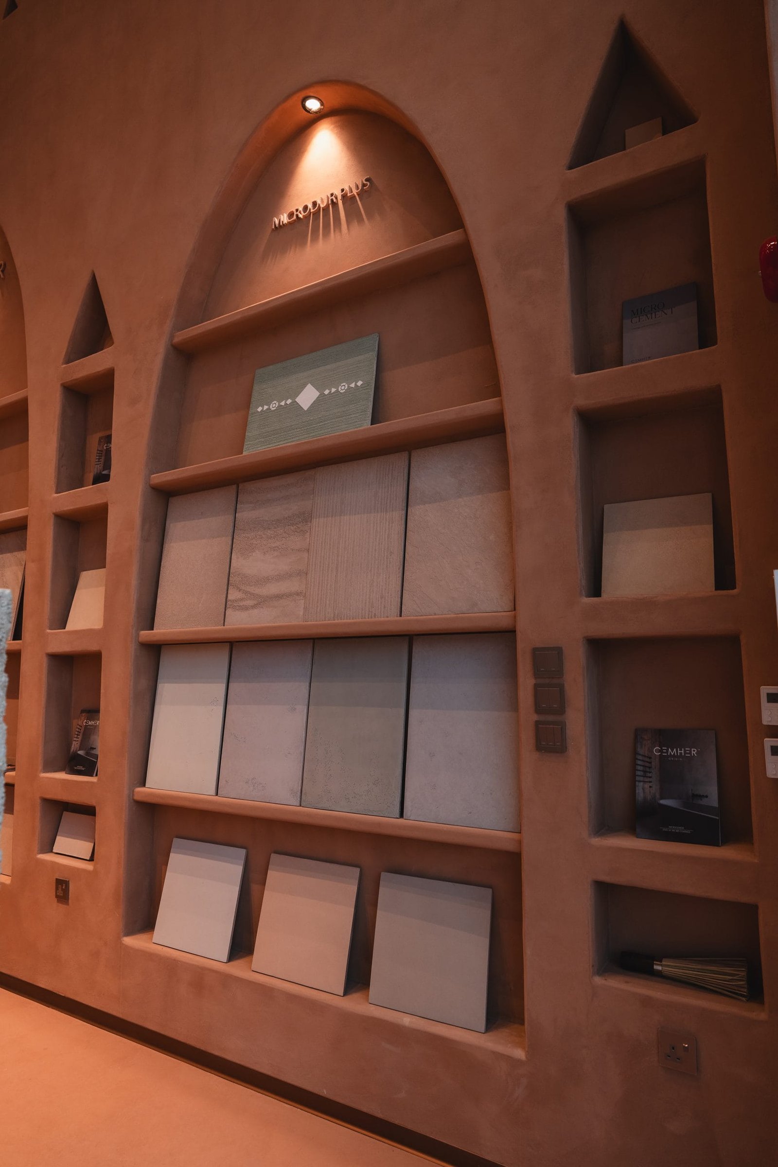 Microdur Plus microcement sample boards on plaster shelves at the Conmarble showroom with Cemher literature alongside.