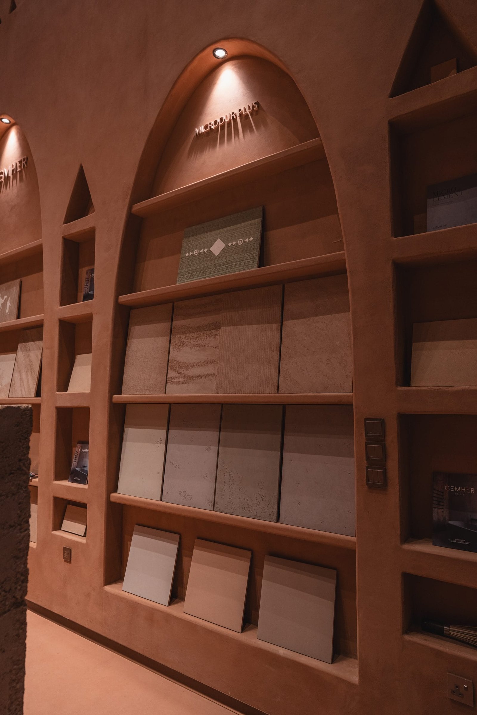 Microdur Plus and Cemher arches at the Conmarble showroom seen from below, sample boards receding under the perforated ceiling.