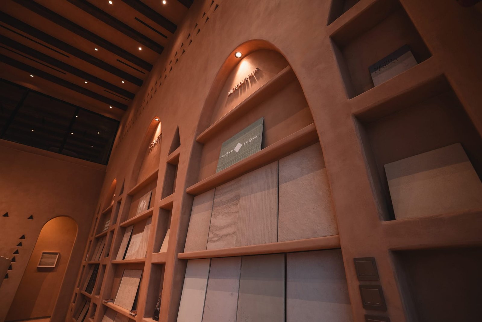Microdur Plus arch at the Conmarble showroom, grey and greige microcement sample boards stepped across plaster shelves.