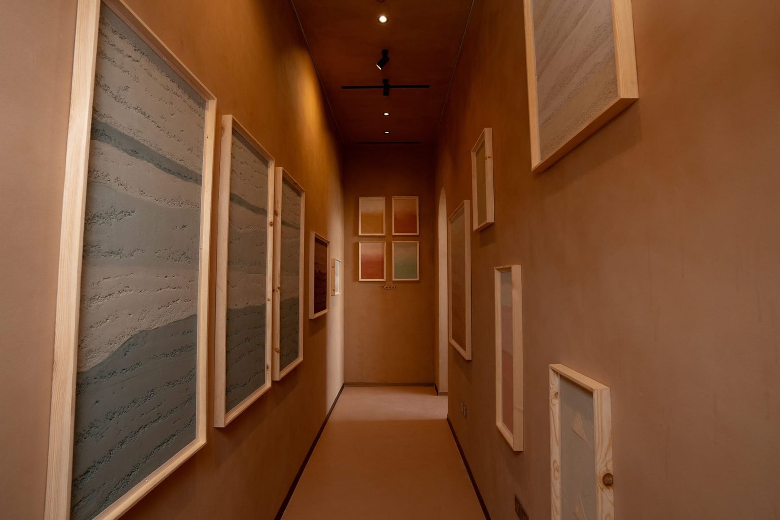 Rammed earth plaster sample gallery corridor at the Conmarble showroom, framed strata panels down both clay-plastered walls under track lighting.