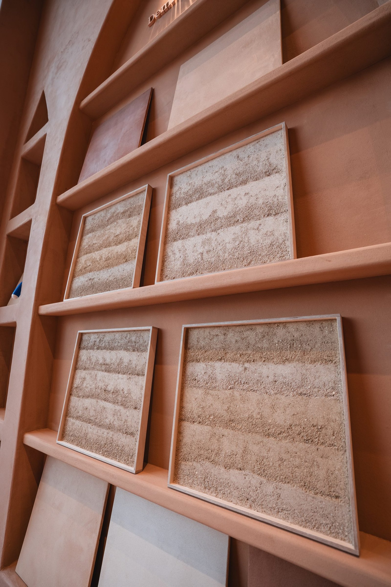 Framed Clayworks Rammed Earth Finish sample panels on plaster shelves at the Earth Layers showroom in Riyadh
