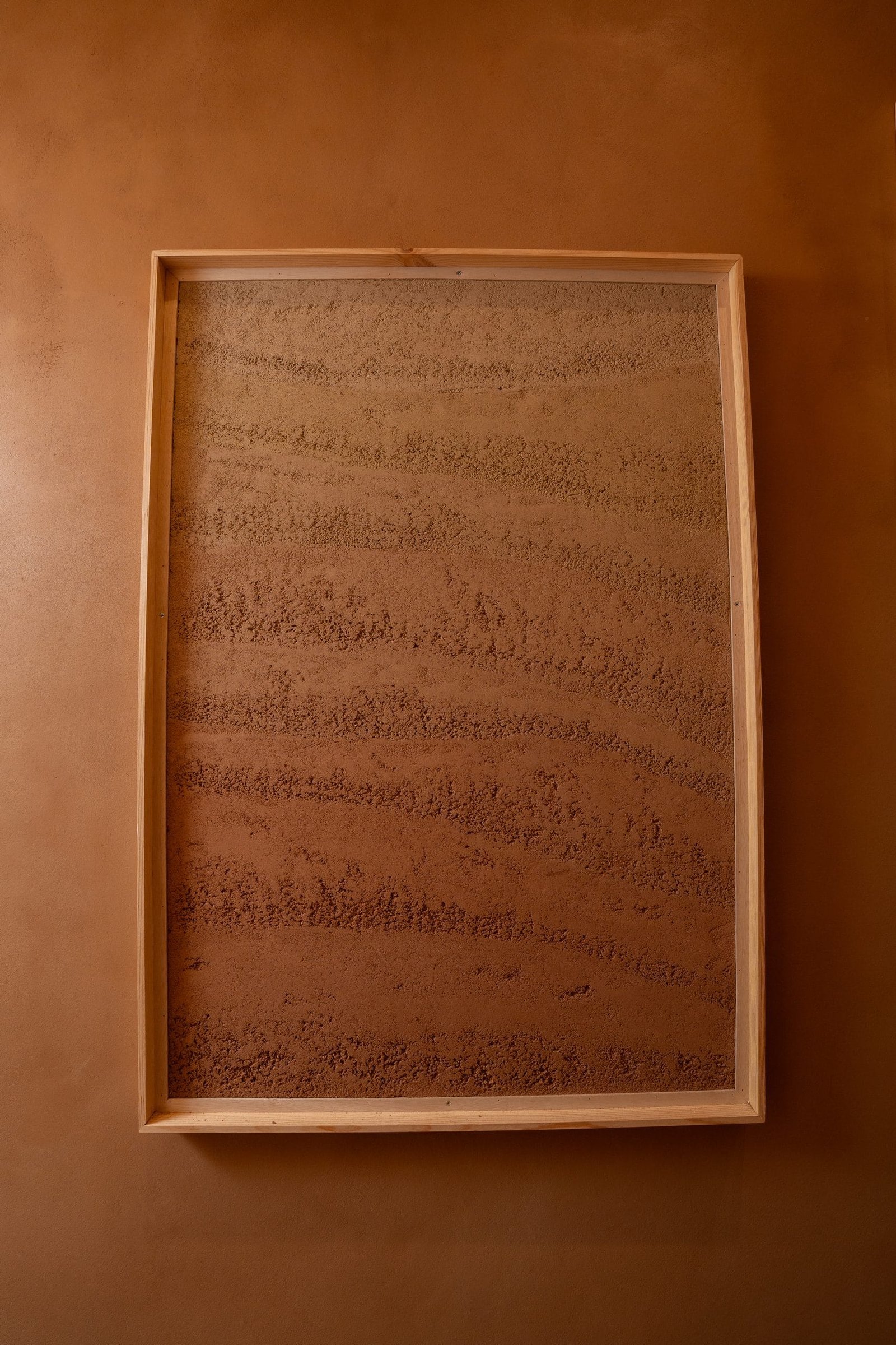 Large framed Rammed Earth Finish plaster sample at the Conmarble showroom, tamped bands running warm ochre to terracotta.