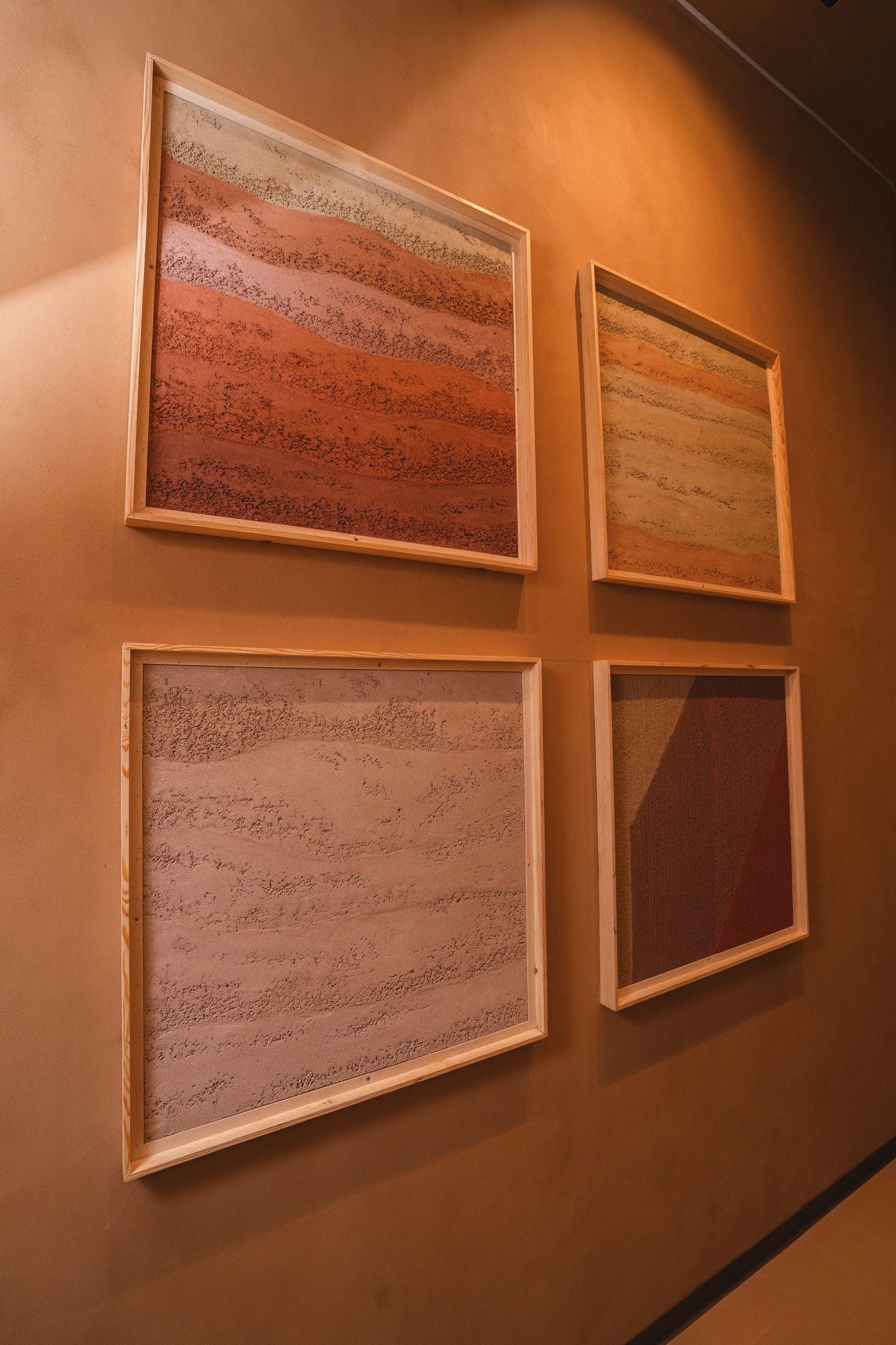 Rammed Earth label above two framed rammed earth plaster panels at the Conmarble showroom, one graded cream to terracotta, one with a curved band.