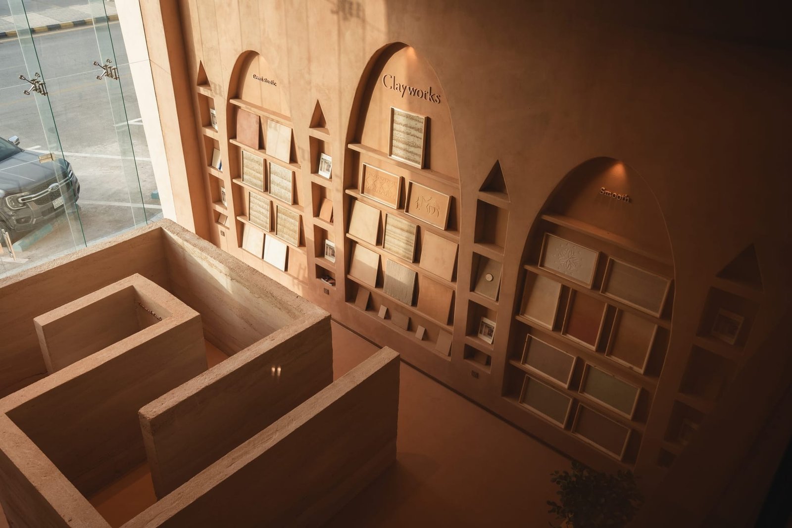Showroom overview at Conmarble Riyadh: the rammed earth reception block, arched sample walls and clay-plastered ceiling in evening light.